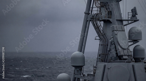 Radar antenna on steel mast of modern warship at sea. Military communication array and electronic warfare system on navy vessel. Strategic maritime defense and naval security technology.