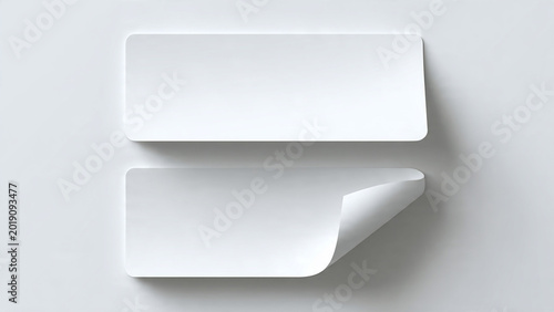 Two white rectangular sticker labels with a curled corner, one flat and one peeling, on a neutral background, perfect for branding mockups, packaging.