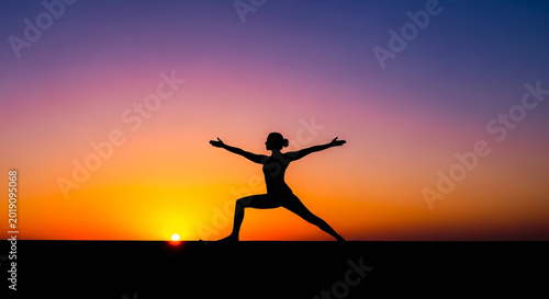 Silhouette of a woman practicing yoga warrior pose at sunset with vibrant sky