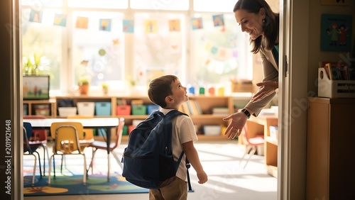 Woman teacher greeting young boy with backpack at classroom door. First day of school student arrival. Elementary education, child care and friendship concept in primary school setting.