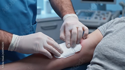 Medical professional applying sterile dressing to patient's arm wound.