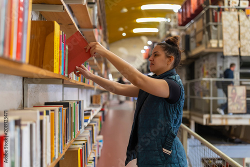 Billede på lærred Woman choosing book from library shelf