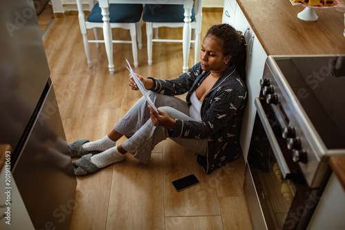 Woman reading bills on kitchen floor at home