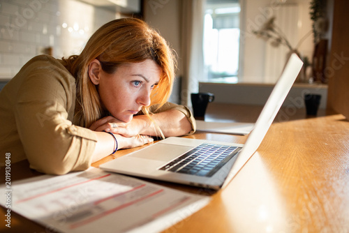 Stressed woman staring at laptop over unpaid bills at home