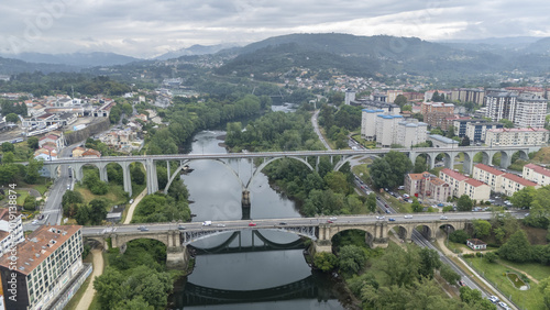 Aerial view of the Ponte Nova bridge and railway viaduct crossing the Minho River surrounded by lush green trees and urban buildings in Orense, Ourense, Spain.