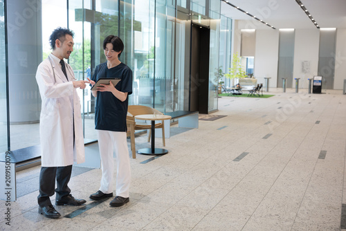 Foto タブレットを見ながら指導や申し送りする医師と新人ドクターや看護師チーム連携イメージ全身