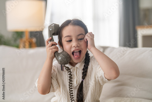 Foto Little happy girl talking on vintage retro telephone sitting on sofa at home, Cu