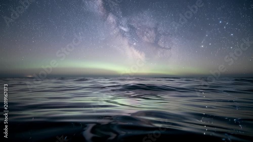 Night sky with Milky Way galaxy over calm ocean water under stars.