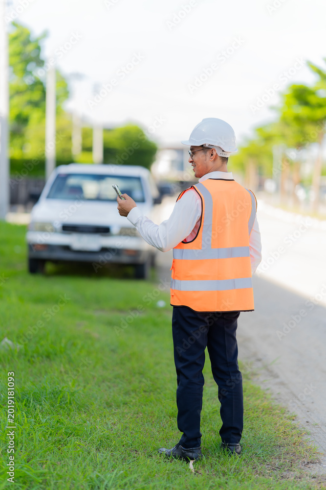 Obraz premium A male civil engineer or construction supervisor, wearing a yellow safety helmet and reflective vest, is on a construction site, representing a real estate development concept for a housing constructi