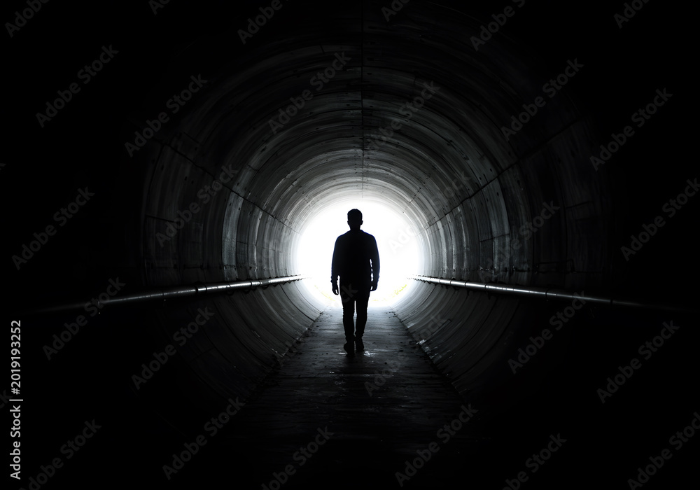 Obraz premium Person walking through dark tunnel towards light