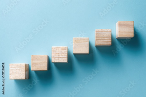 Wooden Blocks Arranged in Ascending Staircase on Blue Background.