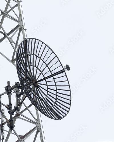 Closeup grid dish antenna attached to cellular communication tower with steel lattice framework, microwave reflector, feedhorn receiver, transmission support brackets and radio telecommunications