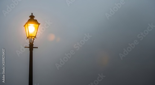 Vintage street lamp glowing in dense fog against a blurred backdrop