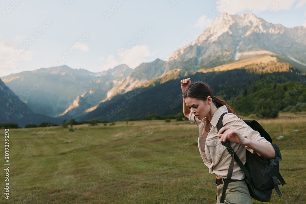 Fototapeta premium Active woman hiking in a mountain valley with a backpack, sunlight on the landscape, outdoors, travel, fitness, nature, adventure, and exploration in a bright, fresh scene.
