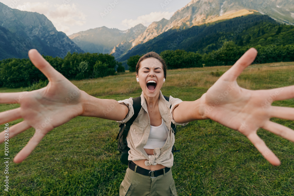 Obraz premium Smiling woman with outstretched arms in a lush valley, mountains in the background. Lifestyle outdoors vibe, happiness, nature, adventure, and travel inspiration.