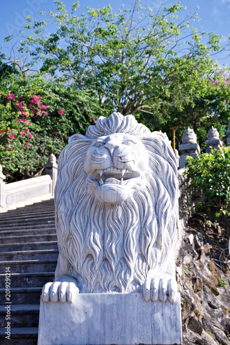 Canvastavla Majestic white marble lion statue guarding a stone staircase in a lush tropical