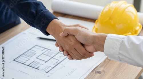 Handshake over architectural blueprint with construction helmet