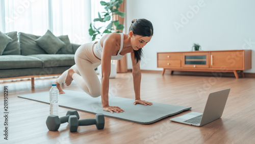 Young Asian woman doing sport exercises indoor. Beautiful girl workout at home. Athletic outfit is doing mountain climber exercises