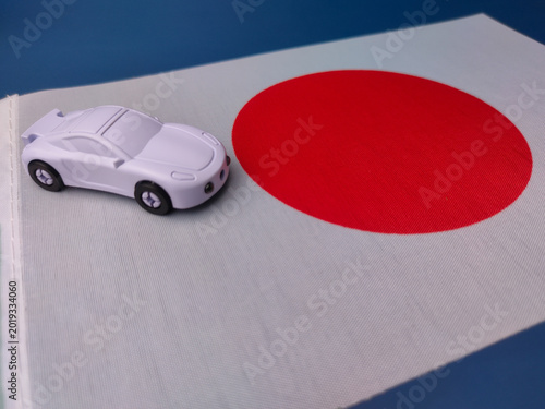 A white toy car is positioned on the white field of the Japanese flag, symbolizing the automotive industry