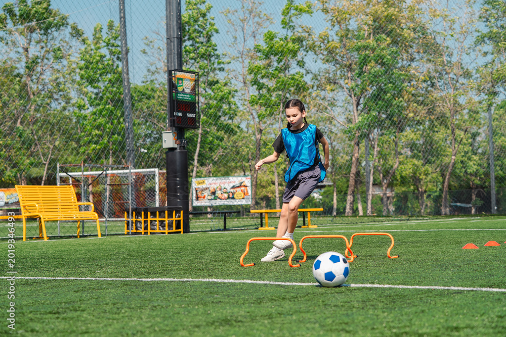Naklejka premium World cup concept with soccer ball or football player, youth soccer player practices hurdle drill on outdoor field in sunny park
