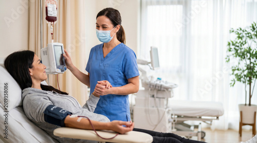 Woman donating blood sample in a medical clinic, attended by a nurse in blue scrubs, with bright natural lighting and a calm, professional atmosphere