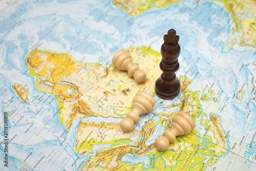 Quadro su tela Black king chess piece standing on a map while white bishops lie fallen, symboli