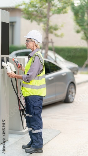 Technician inspecting electric vehicle charging station outdoors