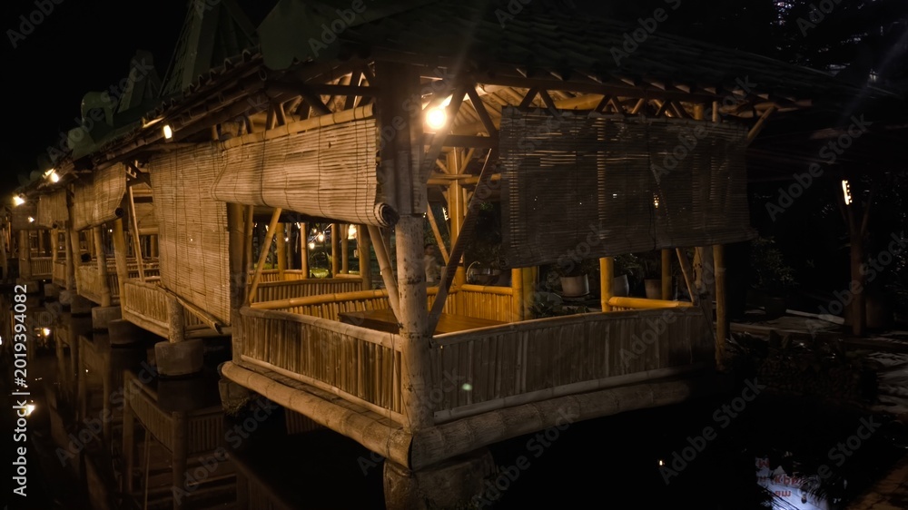 Obraz premium Serene bamboo structure corridor in tropical eco resort illuminated by warm lights at night, elegant wooden architecture, peaceful retreat ambience and relaxing travel scene