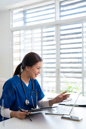 Confident asian doctor talking on video call by looking at camera from hospital with patients. concept of online counseling, medical advice and consultation.