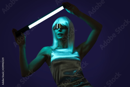 Young woman in futuristic costume with VR glasses and neon lamp on dark backg...