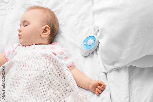 Cute sleeping little baby with radio nanny on bed at home