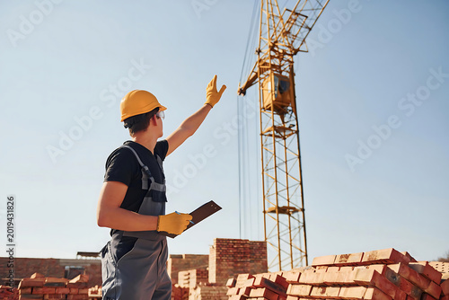 Construction worker signaling crane operator on rooftop under clear sky