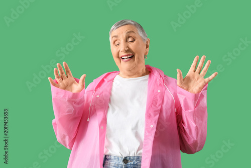 Surprised senior woman in raincoat on green background