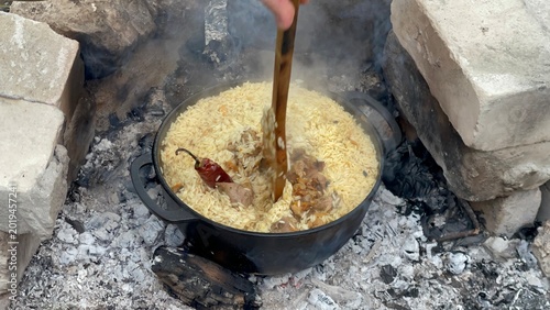 Fotografie Traditional pilaf cooking in a large cast-iron cauldron over an open fire supported by bricks outdoors