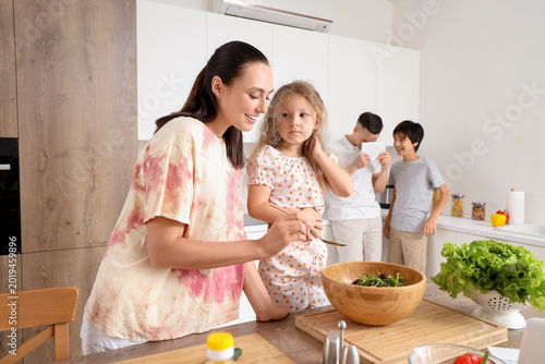 Happy mother with her little daughter cooking vegetable salad in kitchen