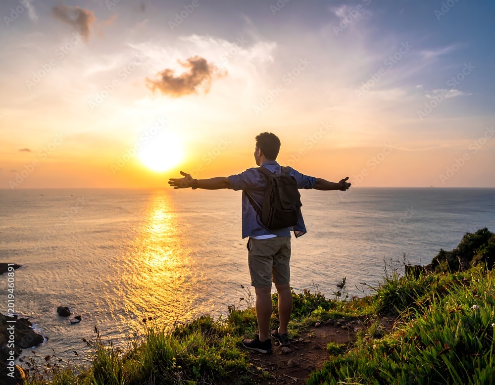 Fototapeta premium A man stands on a cliff overlooking the ocean at sunset