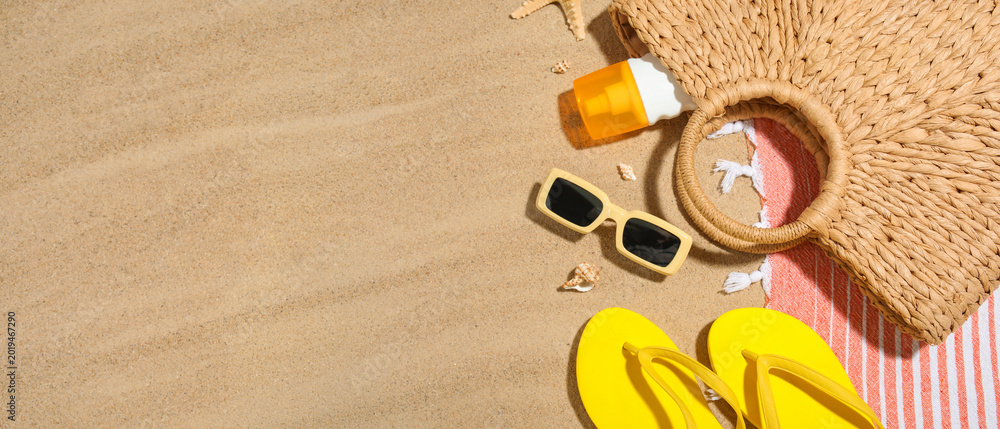 Fototapeta premium Composition with bottle of sunscreen cream, seashells and beach accessories on sand as background, closeup