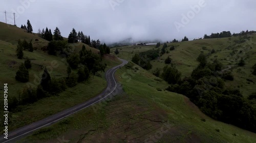 Aerial view of a winding asphalt road snaking through lush green hills under a misty overcast sky in Garberville, California, United States.