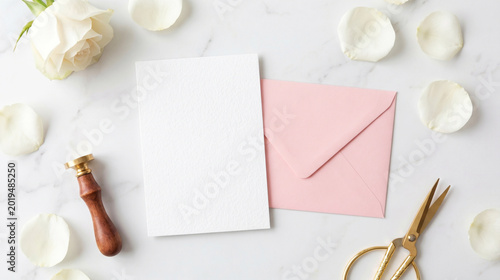 Blank white wedding invitation card mockup with pink envelope rose petals and wax seal on marble background