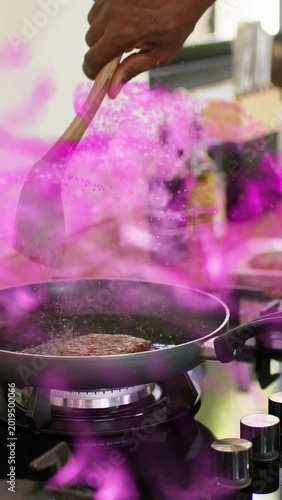 Vertical video: Lit burner heating, senior cook pressing patty for content, pink smoke wrapping pan