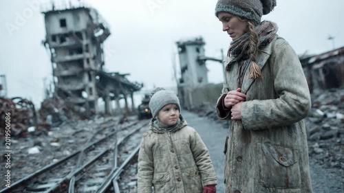 Refugee mother and child walking through the ruins of a destroyed city during a harsh winter