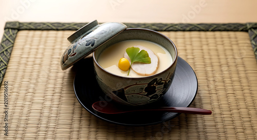 Still life, Zen-inspired. a small, lidded bowl of chawanmushi with a single ginkgo nut and a slice of chicken, the surface perfectly smooth, placed on a woven rush mat (goza)