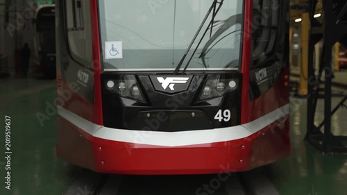 Red modern tram slowly pulls out of the depot during the day. The windshield, headlights, and front of the train