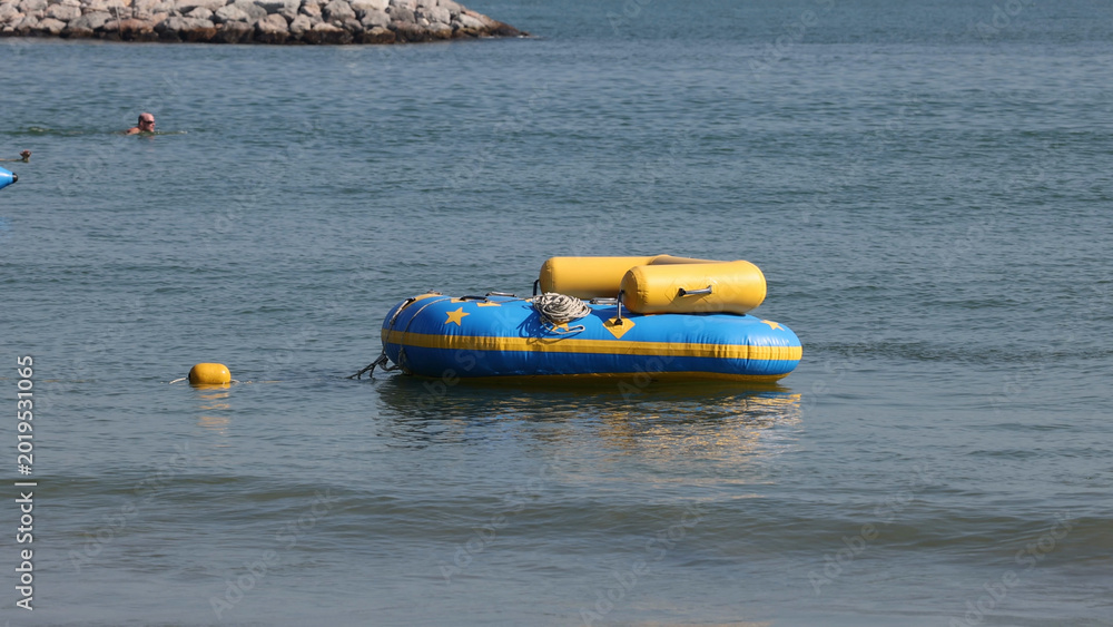 Fototapeta premium Blue and Yellow Inflatable Raft Floating on Calm Water Near Shore