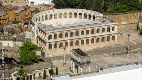 Tablou pe pânză Aerial view of the iconic ancient Roman set at Cinecittà Studios in Rome, Italy, featuring a reconstructed white marble forum with arched colonnades and a triumphal arch, used for epic cinema