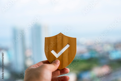 Schilderij op canvas Hand holding wooden shield with checkmark against blurred city background