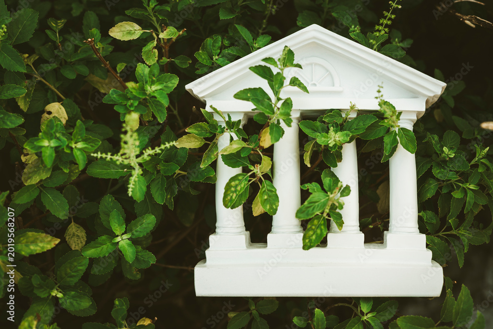 Naklejka premium White bank building model overgrown with green plants. Outdated financial system, abandoned institution, economic crisis, nature reclaiming architecture, and obsolete business concept.