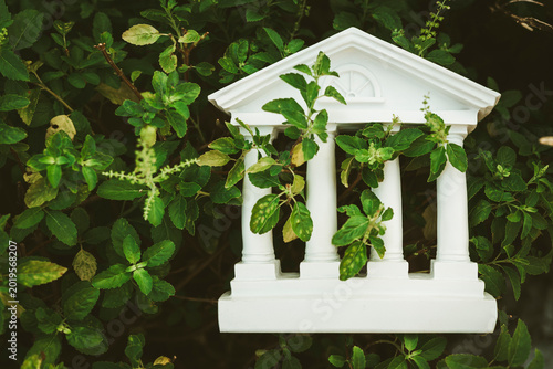 White bank building model overgrown with green plants. Outdated financial system, abandoned institution, economic crisis, nature reclaiming architecture, and obsolete business concept.