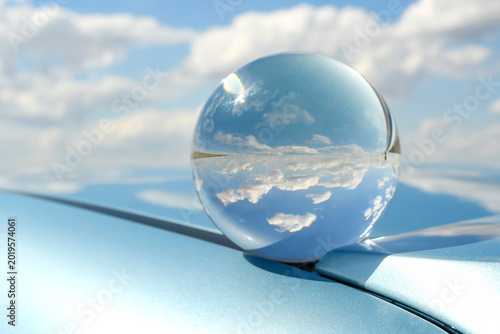 Crystal lensball refracting clean sky and horizon on a blue car hood. Creative photography representing clean energy, future vision, and environment.