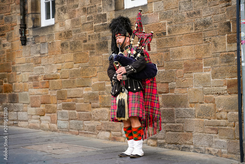 Принти на полотні A bagpiper in traditional Scottish attire in front of a historic stone wall on t